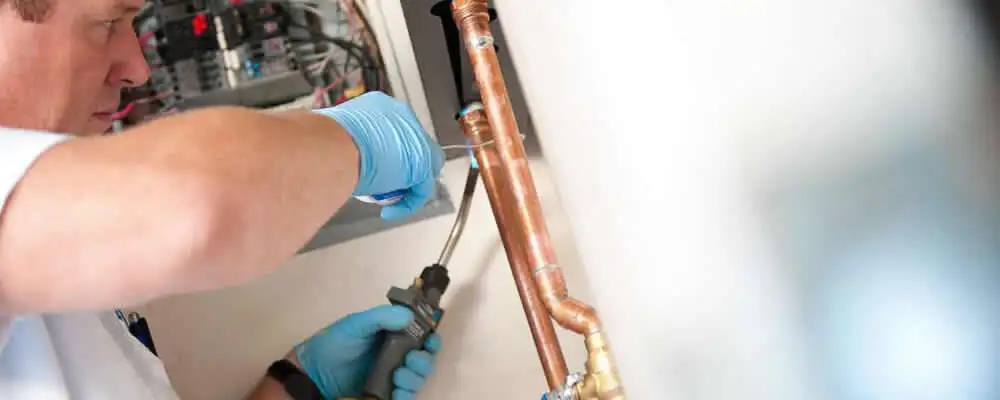 Water heater repair technician testing copper pipe connections and controls in Greensboro, NC